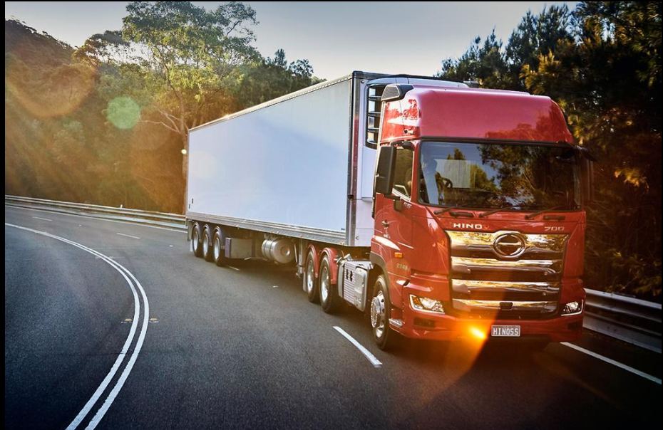 Red Hino 700 prime mover hauling a white box trailer on a winding road