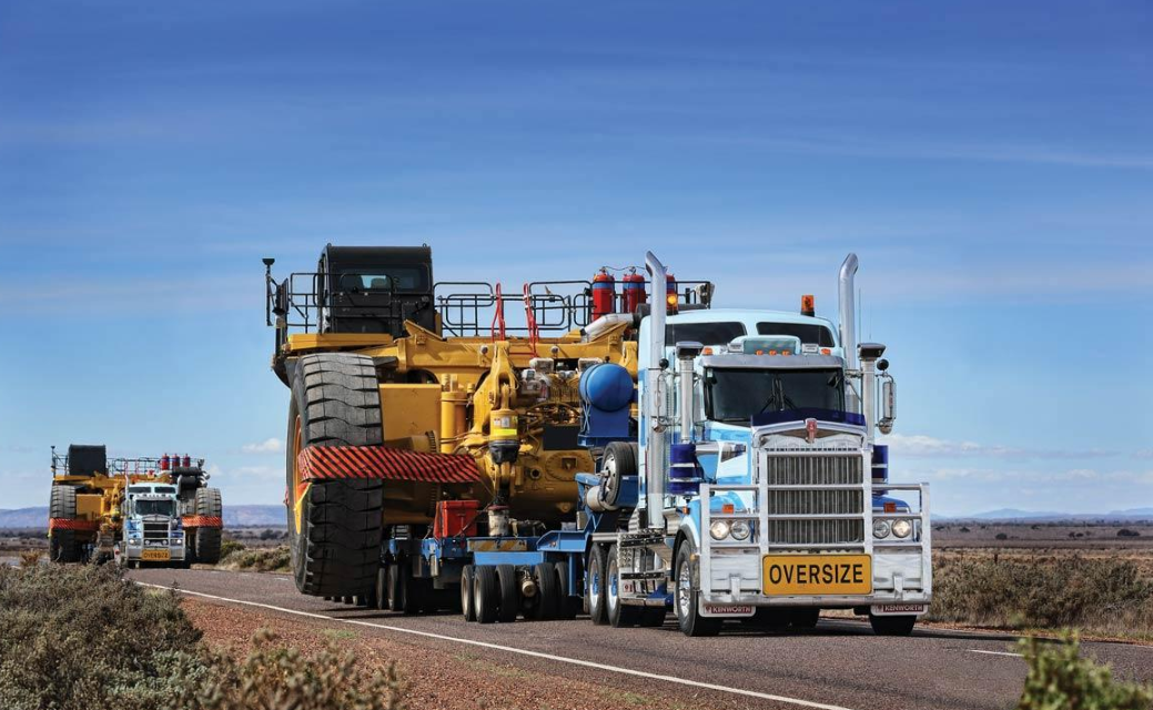 Blue and white Kenworth heavy-haul truck transporting mining equipment